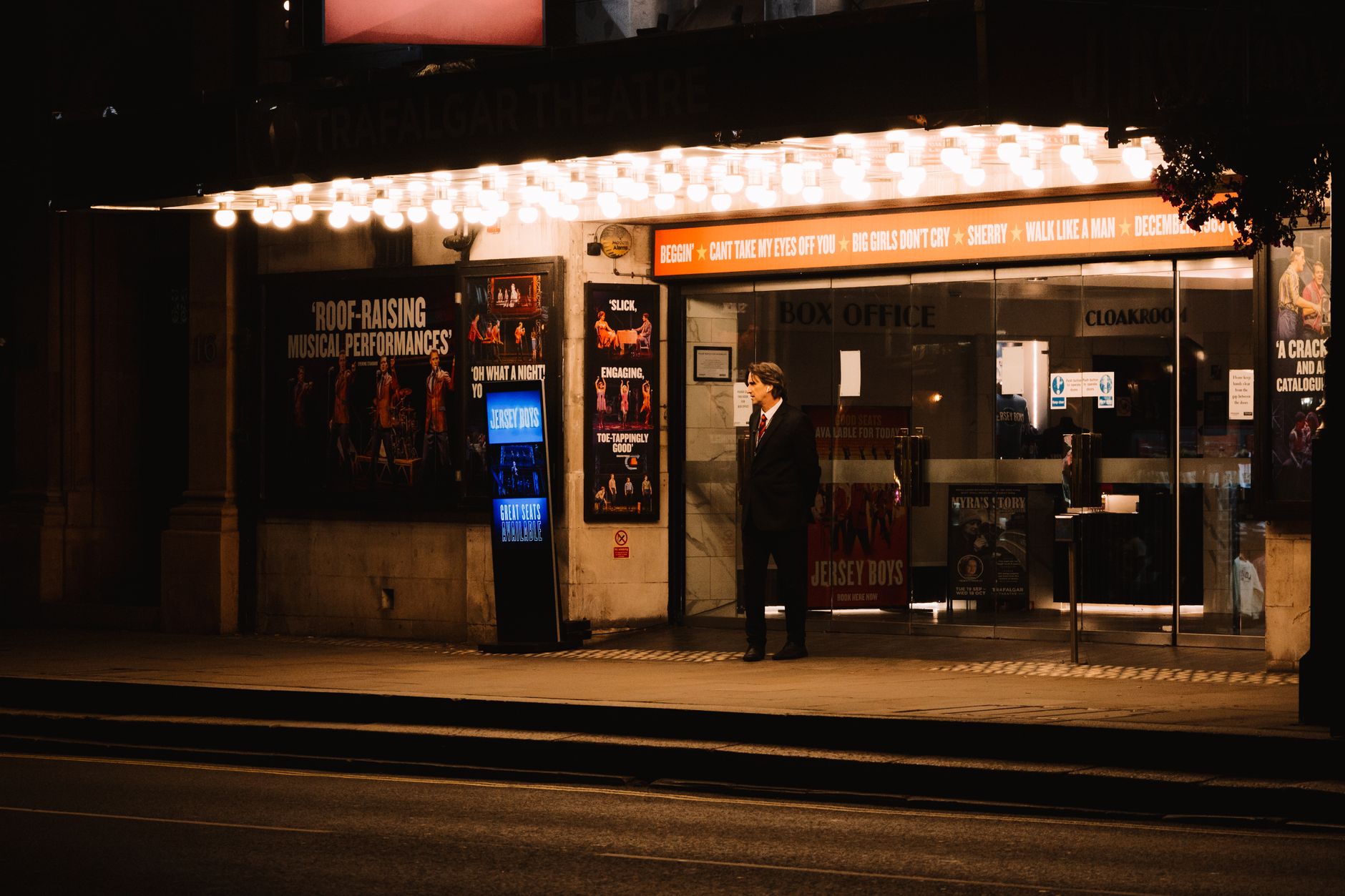 Entrada de teatro iluminada à noite com público chegando